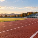 朝日の下に広がる無人の陸上トラックと秋の木立